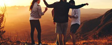 four person standing at top of grassy mountain